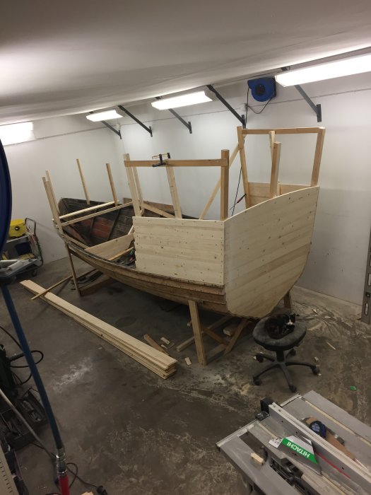 Halvfärdig trähytt under konstruktion i verkstad med lutande framsida och raka sidopaneler.