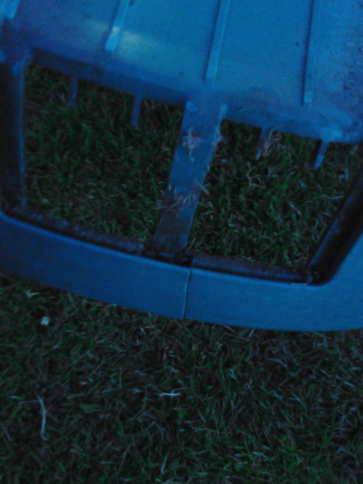 Sprucket robotgräsklipparchassi i första plan mot gräsbakgrund i skymningen.