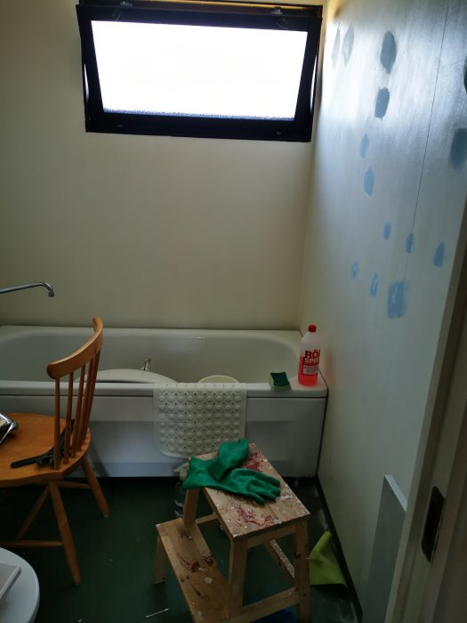 Badrum med bubblor på vägg, badkar, fönster och städmaterial.