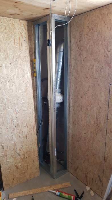 Reglad konstruktion med fläkt och rör i byggprojekt, omgiven av OSB-skivor, med verktyg på golvet.