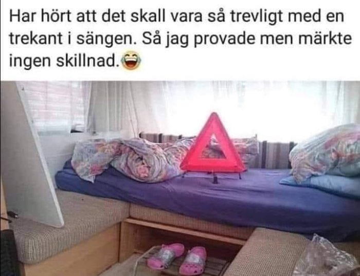 En röd varningstriangel står på en oordnad säng i en husvagn, skämtsam ordlek om trekant.