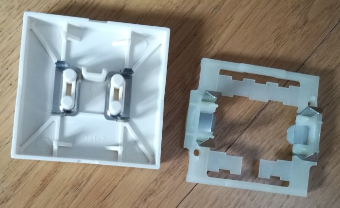 Vit täckram och brytare för elinstallation mot trägolv.