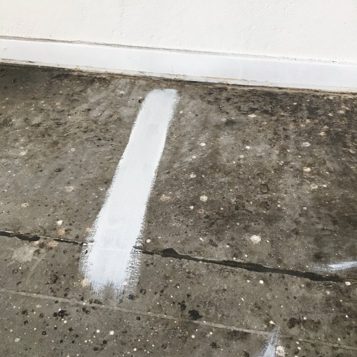 Betonggolv med en teststrimma av vit oljegrund nära en vit vägg.