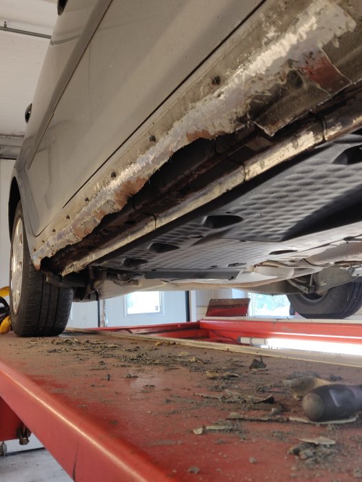 Rostskador och flagnande färg under en grå VW Golf från 2005 som står på en lyft.