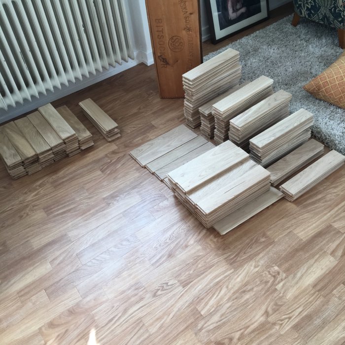 Sorterade trägolvplankor av modellen "Rustik" utlagda på golvet inför läggning.