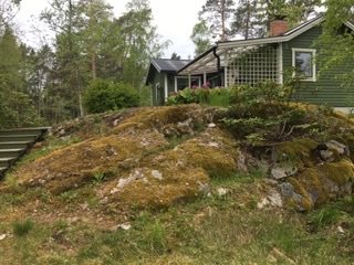 Ovärdad sommarstuga med naturliga bergsknallar och stensatta rabatter i trädgården.