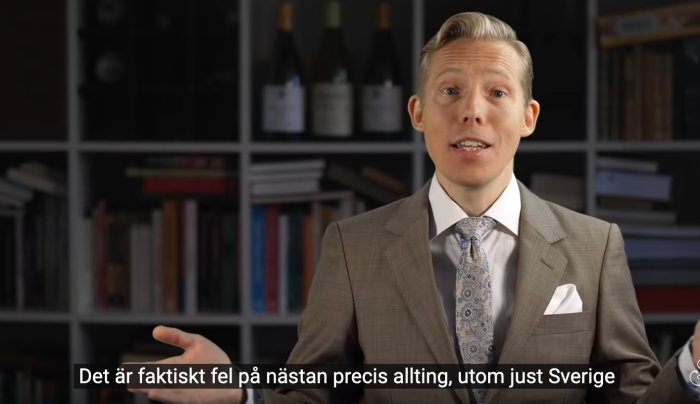 Man i kostym pratar framför bokhylla, svensk textning på videon: "Det är faktiskt fel på nästan precis allting, utom just Sverige".
