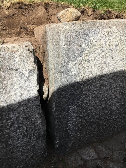 Avstånd mellan stora fyrkantiga stenblock som används som stödmur, med synligt jordläckage.