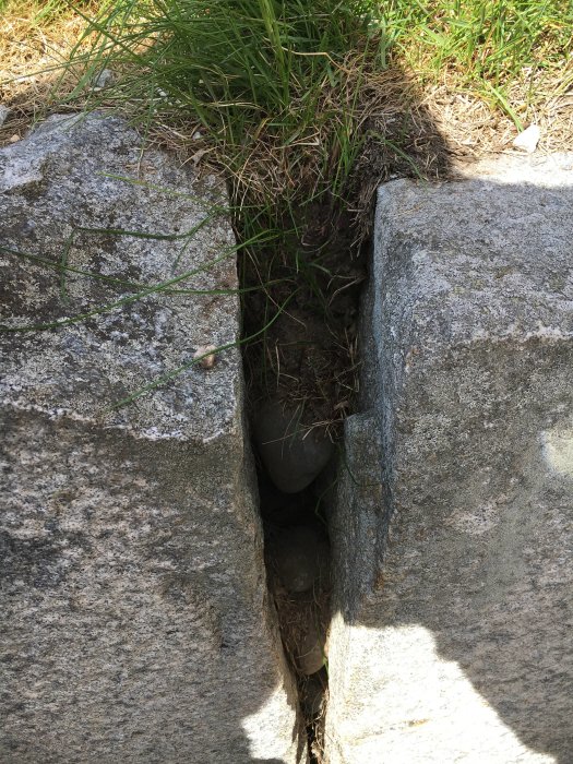 Stort fyrkantigt stenblock som stödmur med mellanrum där jord rinner ut.