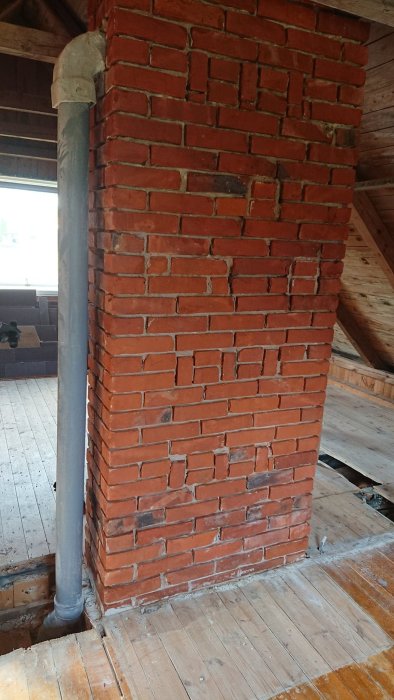 Rörgenomföring i övre del av en murstock på renoverad vind med synlig balk och trägolv.