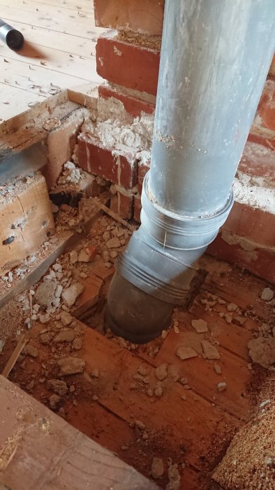 Ventilationsrör går genom upprivet golv och in i gammal murstock omgiven av tegel och träbjälkar.