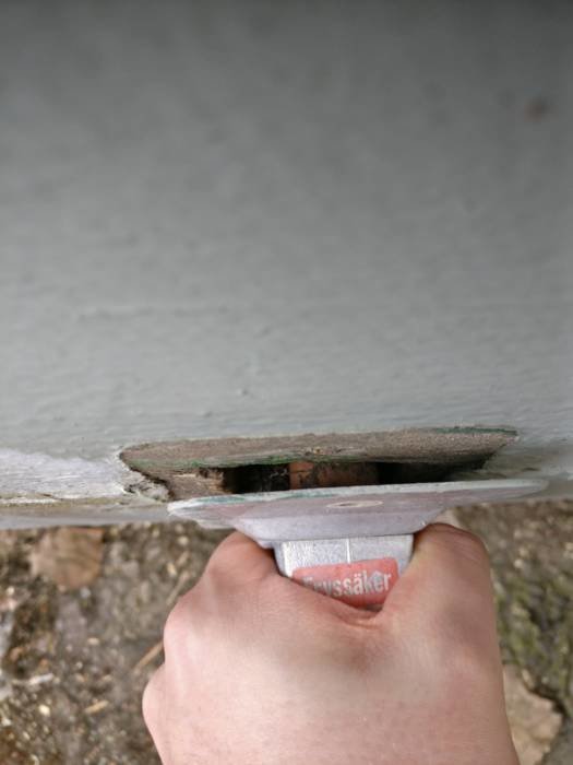 Hand håller en öppen avkastare under en byggnads golv med synliga rör och isolering.