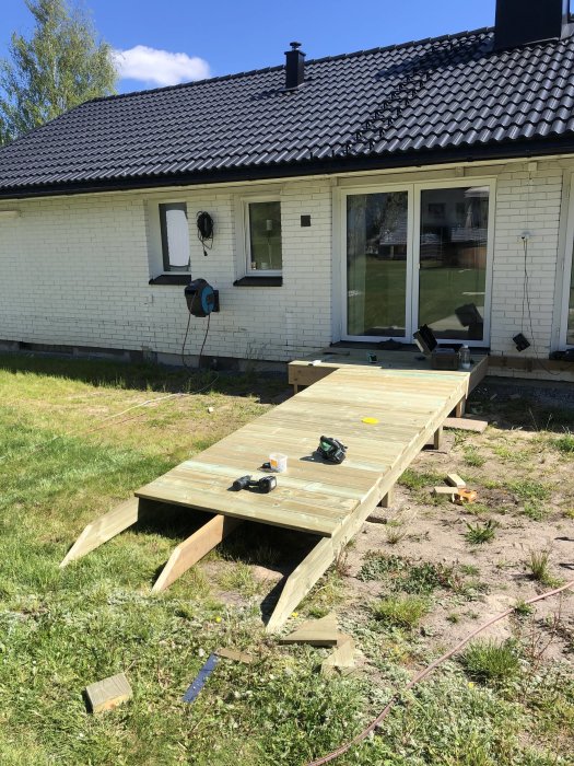 Träkonstruktion som fungerar som temporär brygga från hus till gräsmatta med verktyg ovanpå.