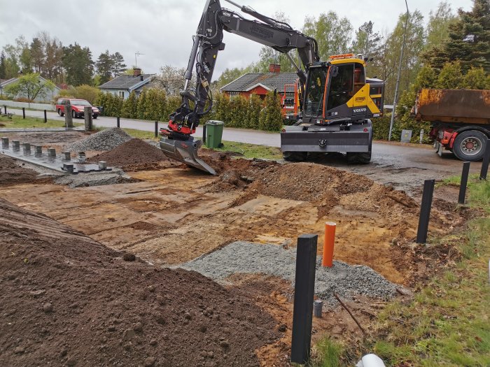 Arbetsplats med grävmaskin och lastbil vid förberedelse för markstenläggning och parkeringsbygge.