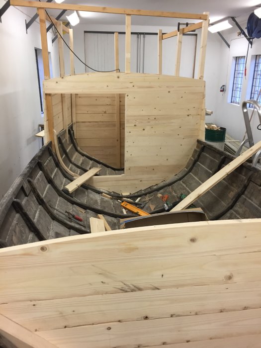 Byggplats med träkonstruktion och en låg dörröppning, omgivet av böjda träspår och verktyg.