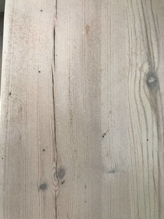 Nyslipat furugolv med vitmattlack som visar sprickor och gulfärgning mellan brädorna.