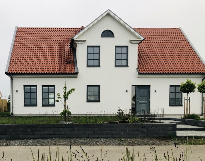 Vit villa med rött tegeltak och symmetrisk fasad med planerade takfönster för barnrum.