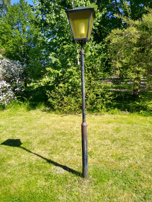 Gammal lyktstolpe i trädgården som liknar de från Narnia, omgiven av grönt gräs och träd.