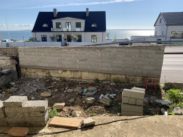 Pågående byggnation av en mur med utsikt över havet, byggmaterial och verktyg synligt.