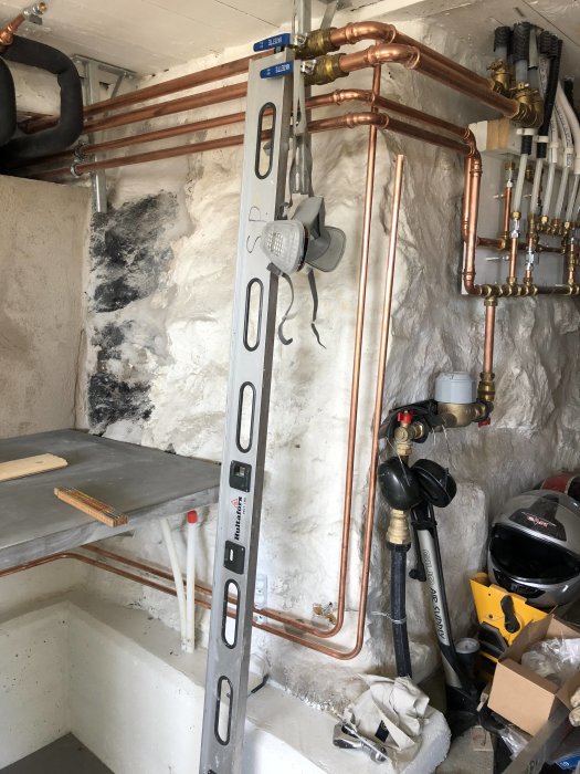 Installation av golvvärmerör och kopplingar på en vägg i ett källarrum med verktyg och material.