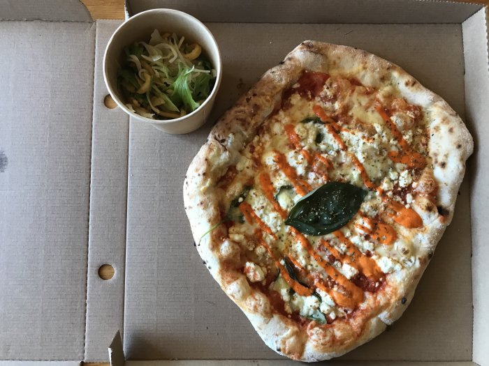 En nybakad pizza i en kartong bredvid en liten skål med sallad.
