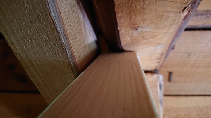 Träkonstruktion där en ny diagonal delvis möter en tjockare träbalk i en taknock.