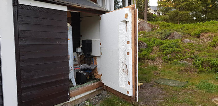 Pumphus med öppen dörr, visar frigolitisolering och delvis synlig pump och hydrofortank bakom.