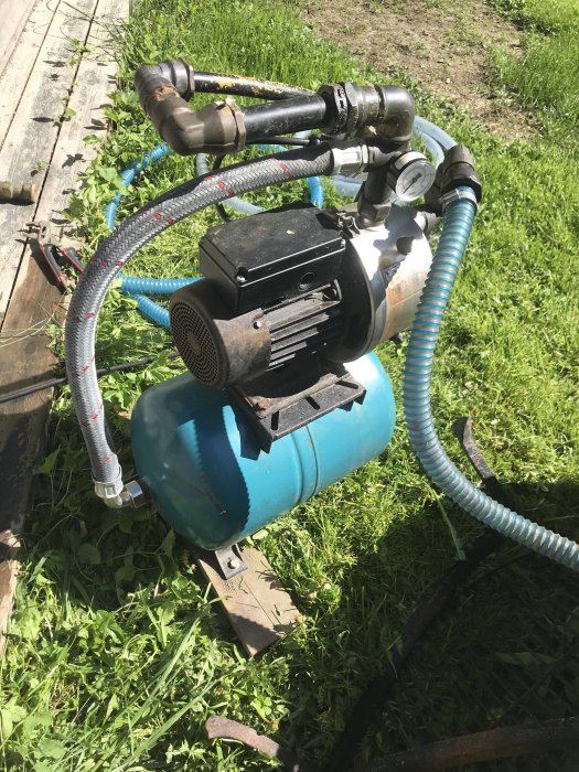 Gamla Grundfos JP5 vattenpump med 20l trycktank och anslutna sugslangar på gräsmatta.