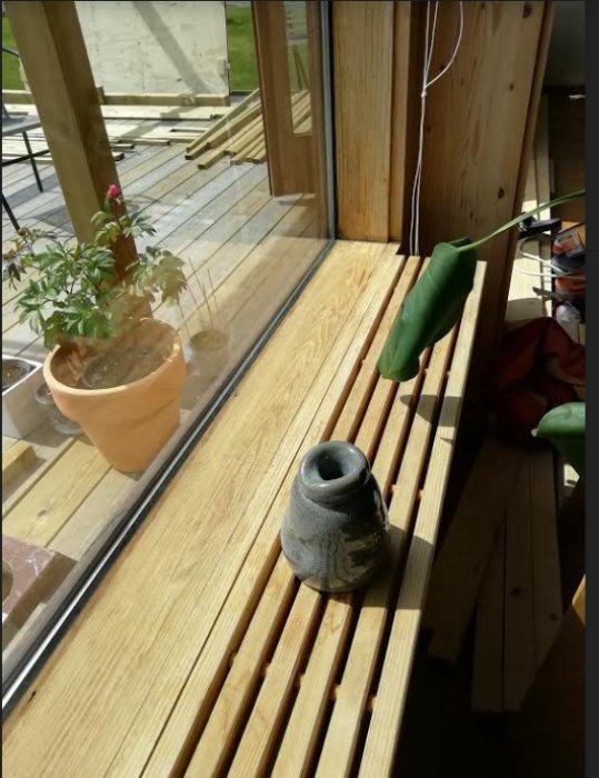 Träfönster med isolerglas i solljus, ådring synlig, utan furukvistar, nära krukväxt och kruka.