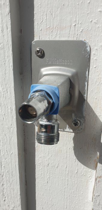 En vattenutkastare från FM Mattsson med en blå övergångskoppling på en vit vägg.