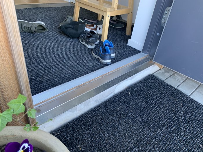 Utsnitt av en ytterdörr och tröskel med västkustskiva och en hög med skor på en grov dörrmatta.