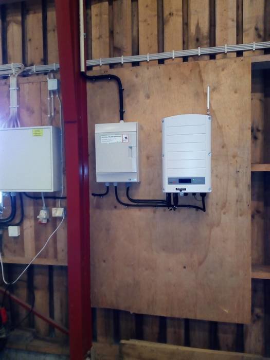 Växelriktare för solpaneler installerad på en trävägg i en maskinhall med rör och elektrisk infrastruktur.