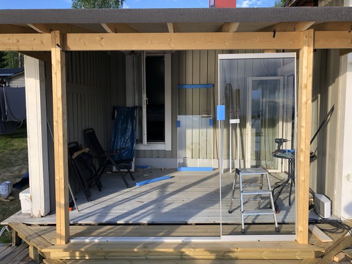 Nybyggt rakt tak över en sned altan med synliga stolpar och en glasdörr i bakgrunden.