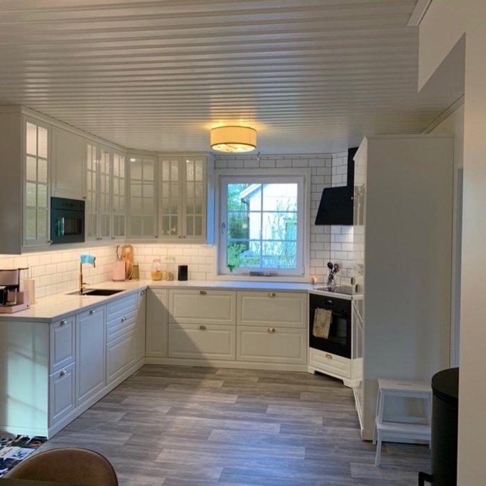 Nyrenoverat kök med vita skåp, kakel och stenbänkskiva, korrekt anpassat efter rummets mått.