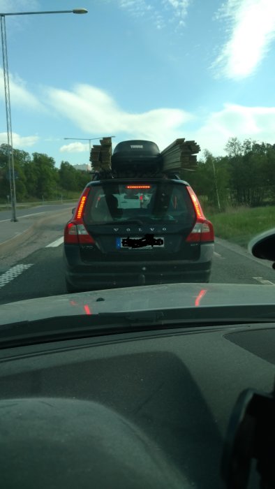 Bil med överlastade brädor på taket och en takbox, säkrade med spännband, på en väg.