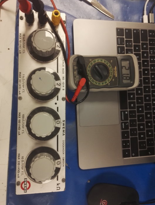 Multimeter visar värde bredvid en bärbar dator och en variabel resistor.