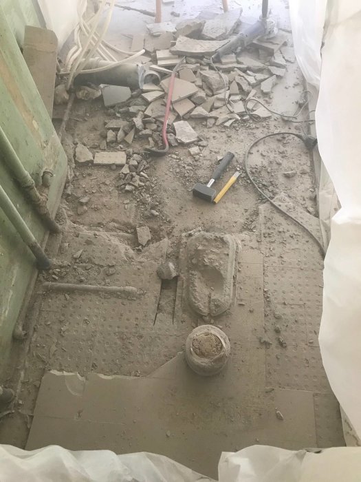 Renoveringsprojekt med rörmokarens verktyg, borttagna klinkerplattor och damm på betonggolv skyddat med plast.