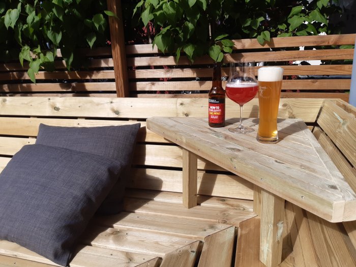 Hemmagjort litet träbord av spillvirke med ett glas öl och en flaska på en solig altan.