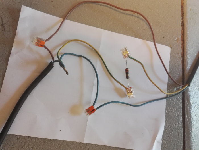 Elkablar med skarvklämmor och en resistor testade i olika konfigurationer ligger på ett papper.