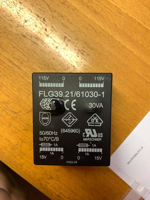 Elektronisk komponent med etiketter och specificeringar, FLG39.21/61030-1, på ett träbord.