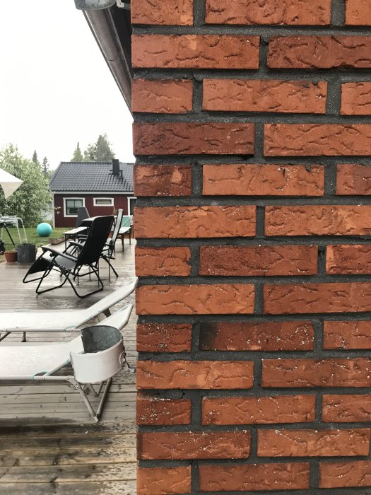 En tegelvägg nära en altan med utsikt mot en trädgård och hus, möjlig infästningspunkt för altantak diskuteras.