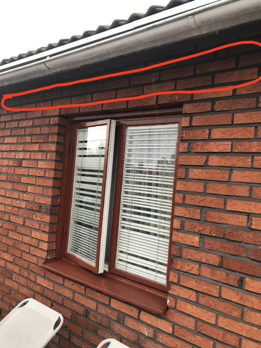 Husfasad med tegelmur, fönster och plåttak där röd linje markerar planerad placering för altantakets bärlina.