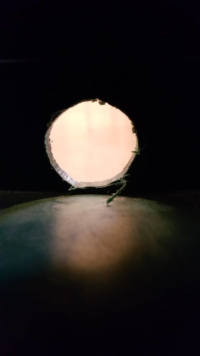 Närbild av ett hål borrat i en vattentunna med synliga kanter och misslyckad kranmontering.
