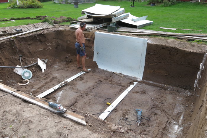 Person tar bort glasfiberpool, verktyg och sand syns i en utgrävd grop i trädgården.