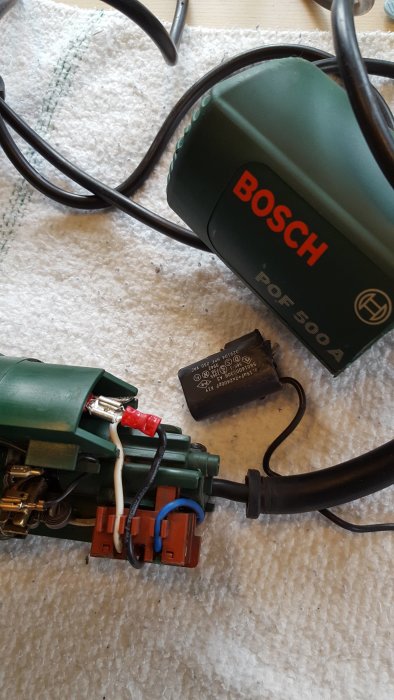 Reparerad Bosch POF 500A fräs med öppet kapsel och synliga ledningar på ett golv.