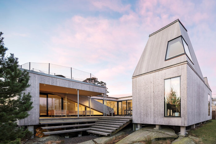 Modern villa med slående arkitektur och träfasad belägen på en klipptomt med utsikt över omgivningen.