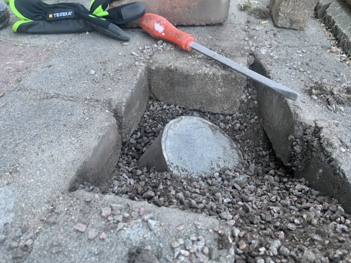 Aluminiumrör slutet synligt under betongsten med grus och mejsel i en upplyft stenläggning.