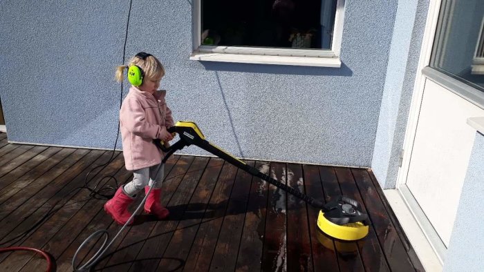 Barn använder högtryckstvätt för att rengöra altandäck i soligt väder.