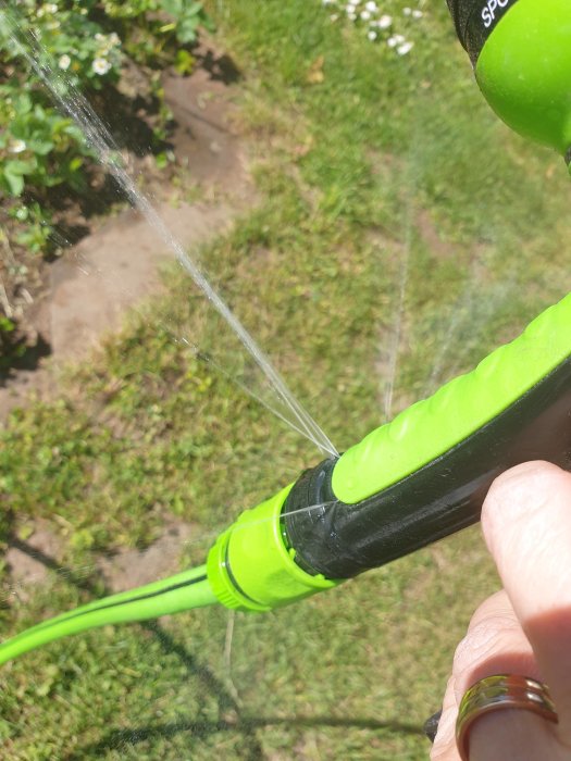 Närbild av en grön vattenslang med vattenläckage sprutandes ut från sidan.