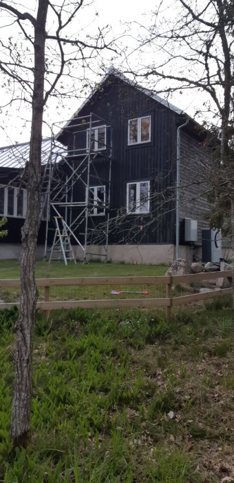 Hus med stående svarta träpaneler på gaveln och byggnadsställning framför.